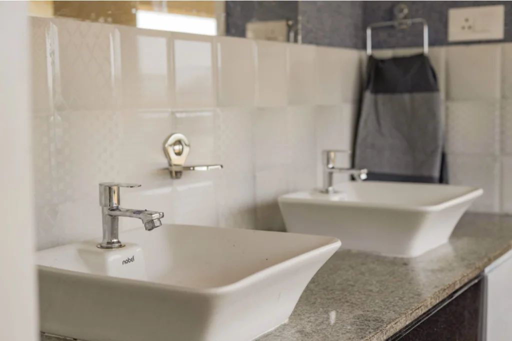 Modern attached bathroom with twin ceramic basin vanity, chrome faucets, and tiled walls