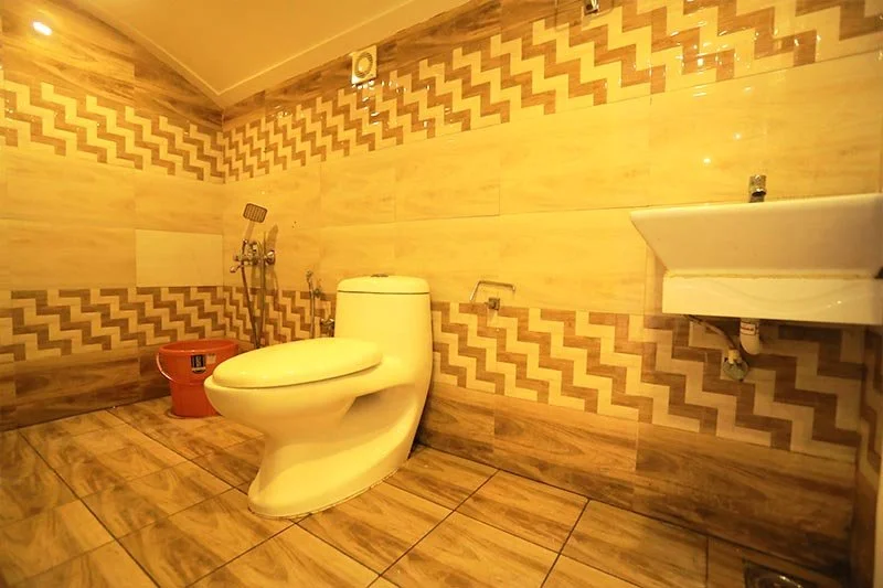 Modern en-suite bathroom with curved western commode, ceramic sink, zigzag ceramic tiles, and wood-grain flooring